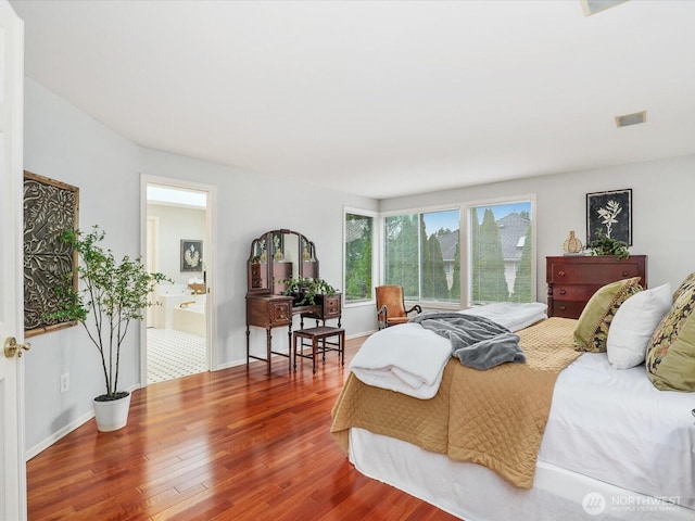 bedroom featuring baseboards, visible vents, wood finished floors, and ensuite bathroom