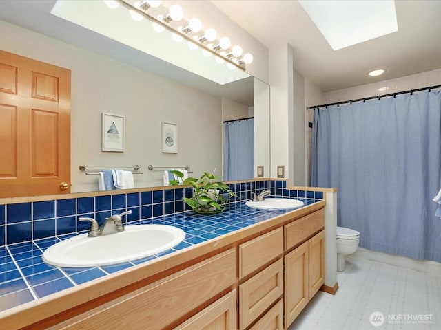 bathroom featuring double vanity, a skylight, a sink, and toilet