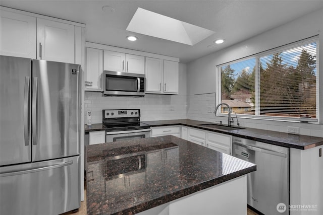 kitchen featuring a kitchen island, appliances with stainless steel finishes, a sink, white cabinetry, and backsplash