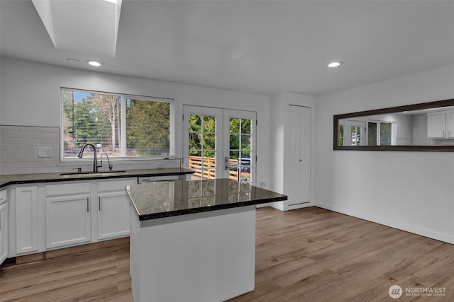 kitchen with a wealth of natural light, dark stone counters, a sink, and light wood finished floors