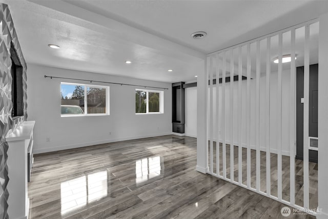 unfurnished room with recessed lighting, visible vents, a wood stove, wood finished floors, and baseboards