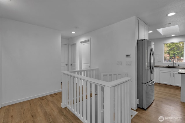 hall featuring light wood-type flooring, a skylight, a sink, and an upstairs landing