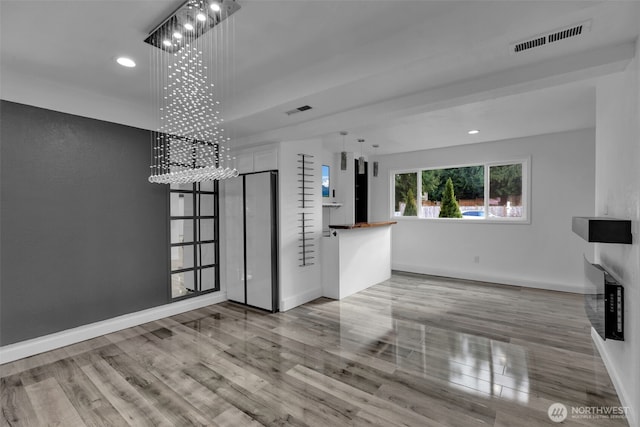 unfurnished living room featuring an inviting chandelier, visible vents, baseboards, and wood finished floors