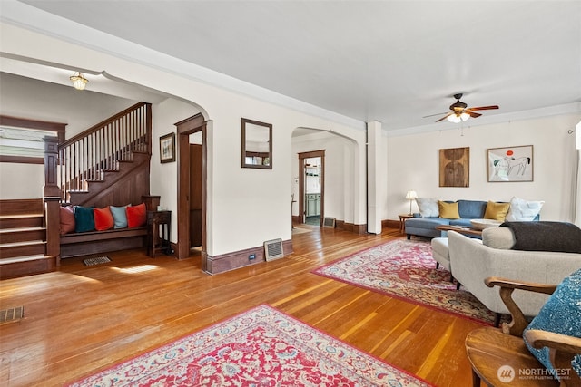 living area with visible vents, stairway, wood finished floors, arched walkways, and a ceiling fan