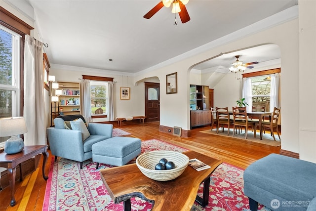 living area with arched walkways, plenty of natural light, and wood finished floors