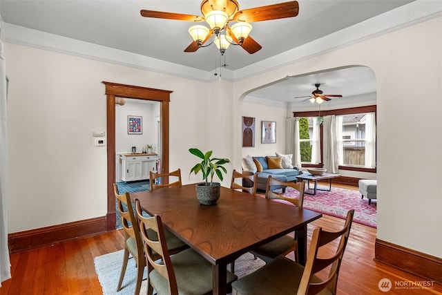 dining room with arched walkways, ornamental molding, baseboards, and hardwood / wood-style floors