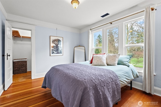 bedroom featuring a closet, a walk in closet, baseboards, and wood finished floors