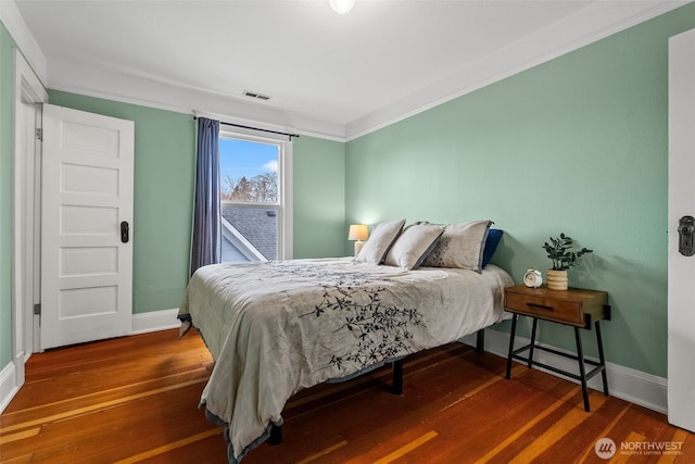 bedroom featuring visible vents, crown molding, baseboards, and wood finished floors