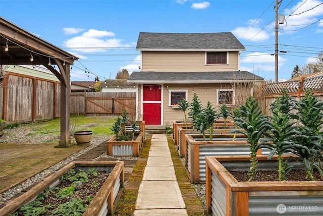 view of front of house featuring roof with shingles, a fenced backyard, and a garden