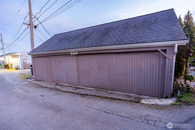 view of side of home featuring a shingled roof and an outdoor structure