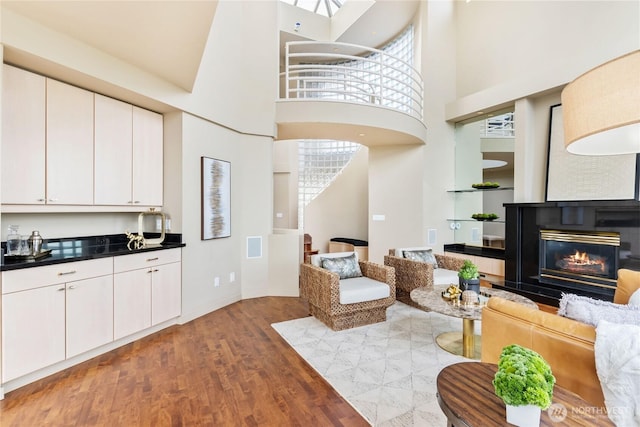 living room featuring a glass covered fireplace, a healthy amount of sunlight, a towering ceiling, and wood finished floors