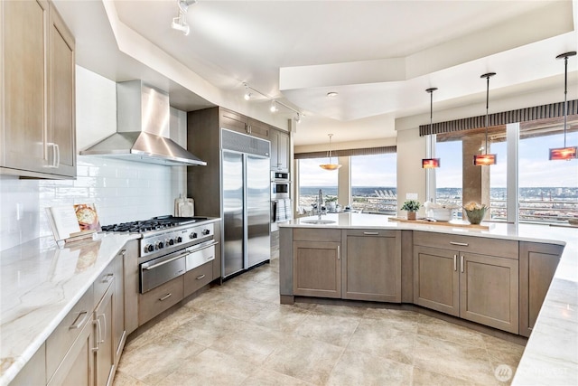 kitchen with tasteful backsplash, appliances with stainless steel finishes, a sink, light stone countertops, and wall chimney exhaust hood