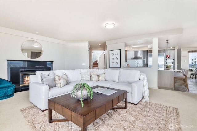 carpeted living area featuring a glass covered fireplace and stairs