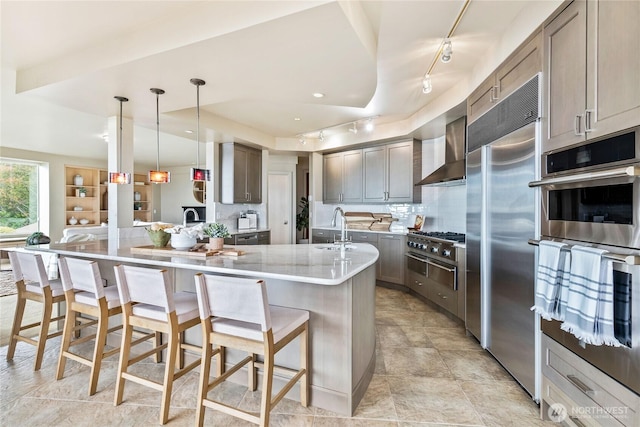 kitchen featuring a breakfast bar area, a sink, wall chimney range hood, appliances with stainless steel finishes, and backsplash