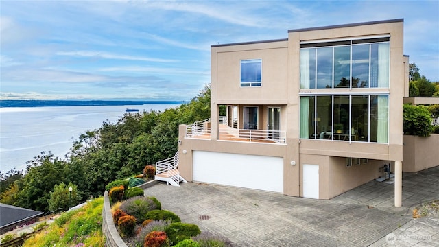 contemporary home with a water view, driveway, a balcony, and stucco siding