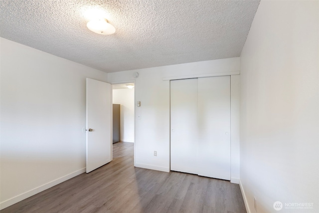 unfurnished bedroom with a textured ceiling, a closet, wood finished floors, and baseboards