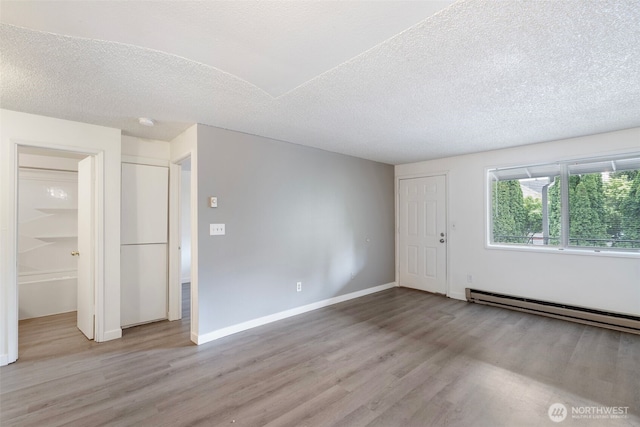 empty room with baseboards, a textured ceiling, baseboard heating, and wood finished floors