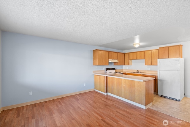 kitchen with white appliances, a peninsula, light countertops, under cabinet range hood, and a sink