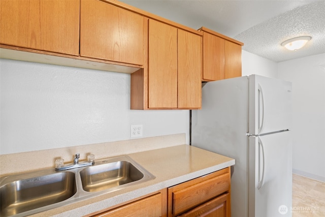 kitchen with a textured ceiling, light countertops, a sink, and freestanding refrigerator