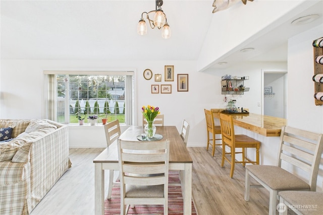 dining room with light wood-style floors, a notable chandelier, vaulted ceiling, and baseboards