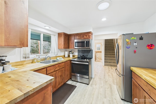 kitchen featuring brown cabinetry, light wood-style flooring, butcher block countertops, appliances with stainless steel finishes, and a sink