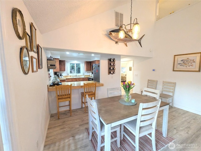 dining room featuring light wood-style floors, visible vents, vaulted ceiling, and a textured ceiling