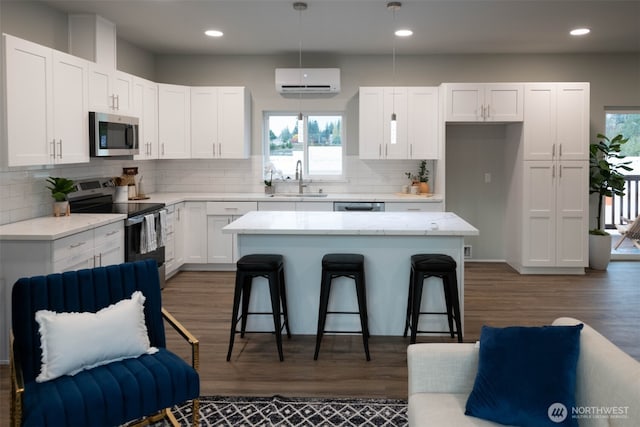 kitchen with appliances with stainless steel finishes, white cabinetry, a sink, a wall mounted air conditioner, and a kitchen breakfast bar