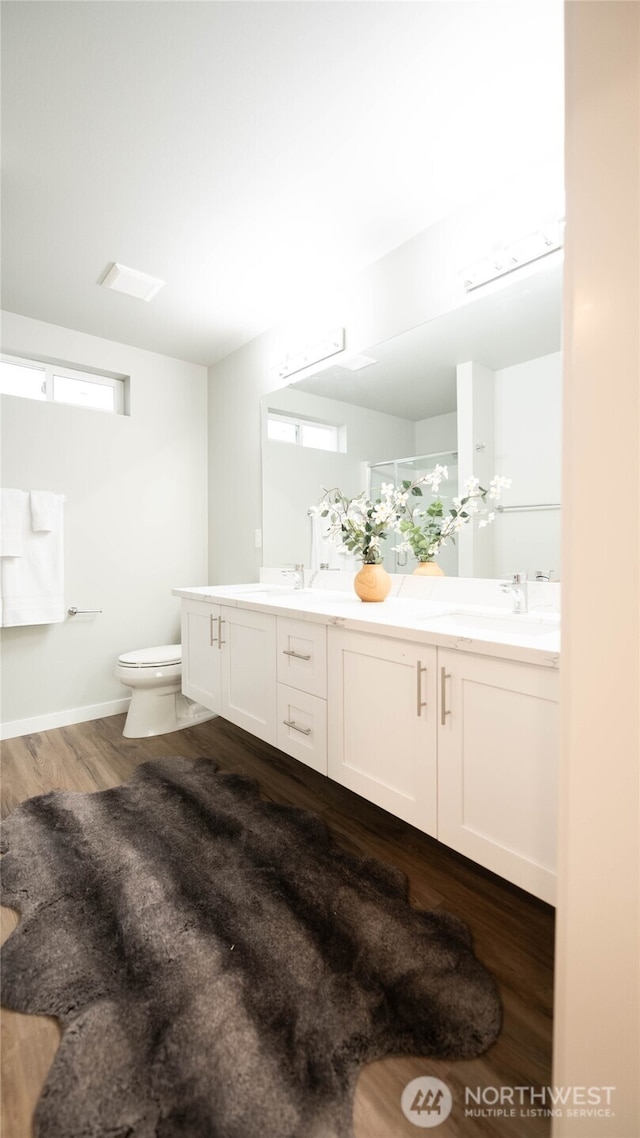 bathroom featuring toilet, double vanity, a sink, and wood finished floors