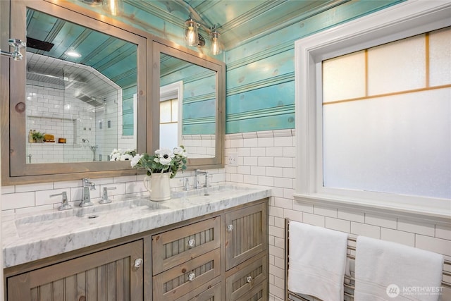 full bathroom with tile walls, a sink, a shower stall, and double vanity