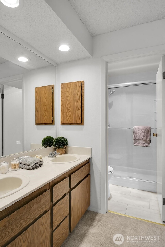 bathroom with double vanity, toilet, a stall shower, a sink, and a textured ceiling