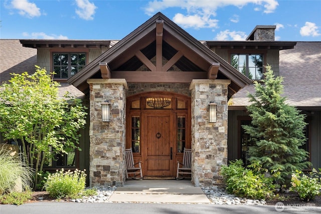 view of exterior entry with stone siding, roof with shingles, and a chimney