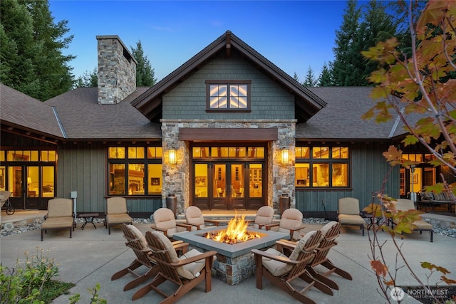 back of property featuring roof with shingles, a chimney, a fire pit, and a patio