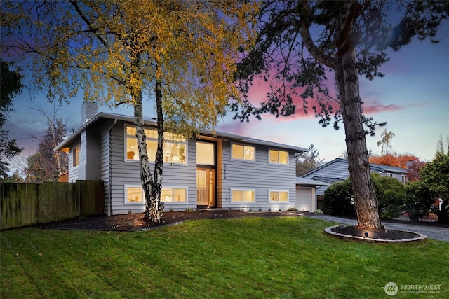 raised ranch featuring a chimney, a front yard, fence, a garage, and driveway