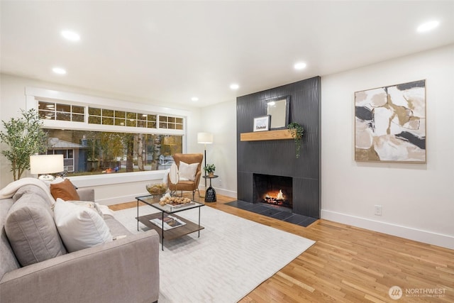 living area with a large fireplace, baseboards, wood finished floors, and recessed lighting