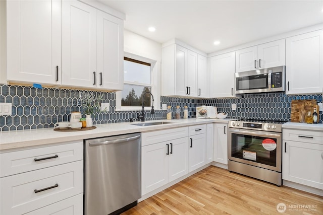 kitchen featuring stainless steel appliances, a sink, white cabinetry, light countertops, and light wood finished floors