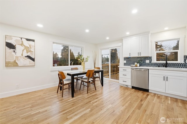 kitchen with light wood finished floors, tasteful backsplash, stainless steel dishwasher, white cabinetry, and a sink