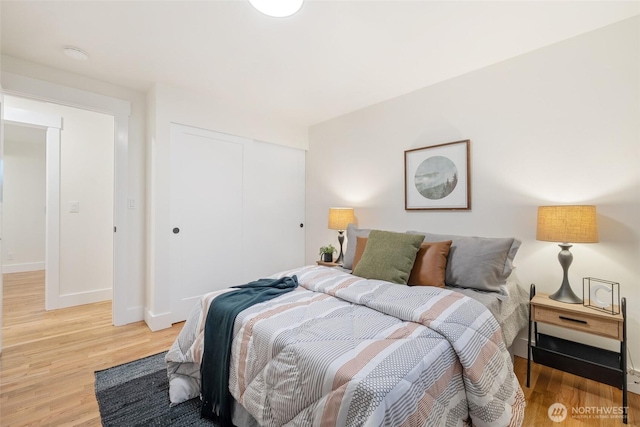 bedroom with light wood-type flooring, baseboards, and a closet