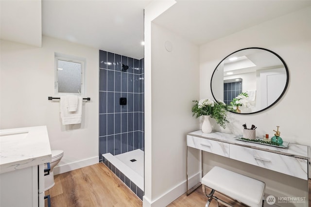 bathroom with wood finished floors, tiled shower, and vanity