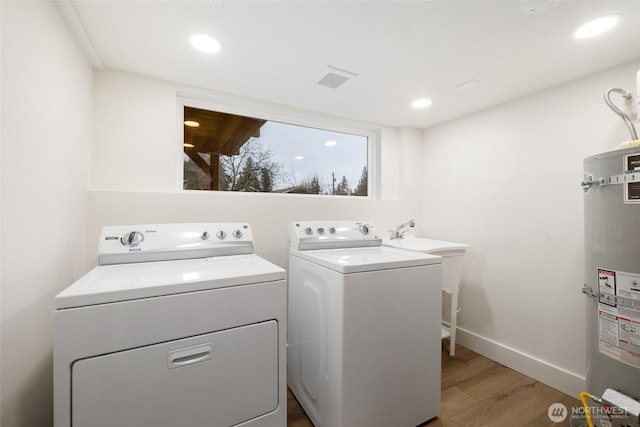 clothes washing area with laundry area, light wood-style flooring, water heater, and washing machine and clothes dryer