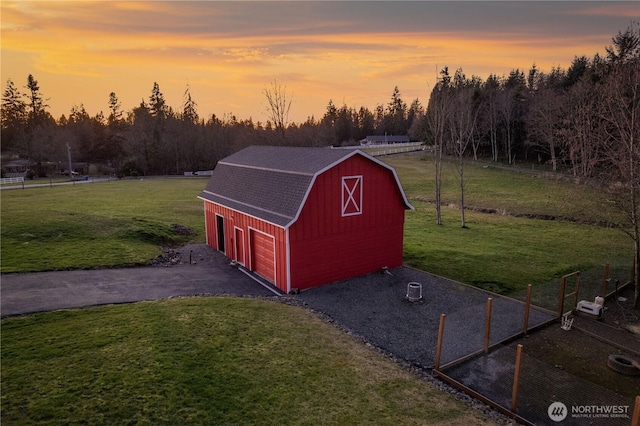 view of barn featuring aphalt driveway, a lawn, and fence