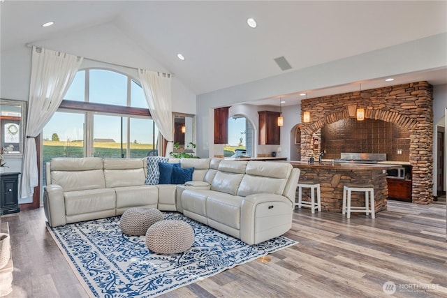 living area with arched walkways, high vaulted ceiling, wood finished floors, and recessed lighting