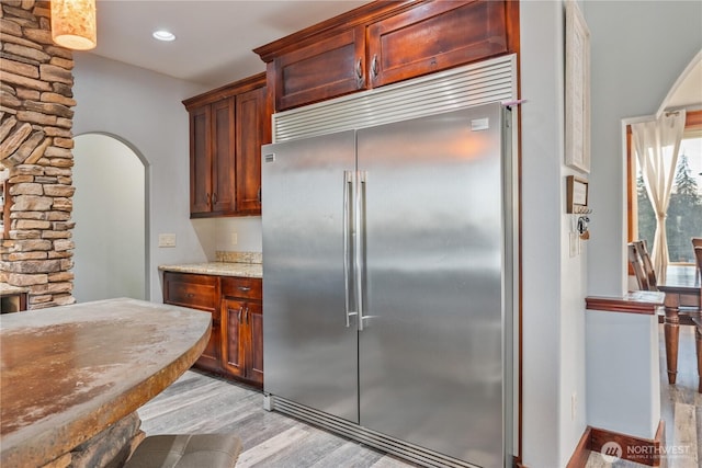 kitchen featuring light stone counters, arched walkways, recessed lighting, light wood-style floors, and stainless steel built in fridge