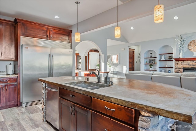 kitchen featuring light wood-type flooring, stainless steel built in refrigerator, a sink, and decorative light fixtures