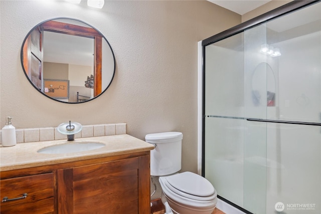 bathroom featuring a textured wall, a shower stall, toilet, and vanity