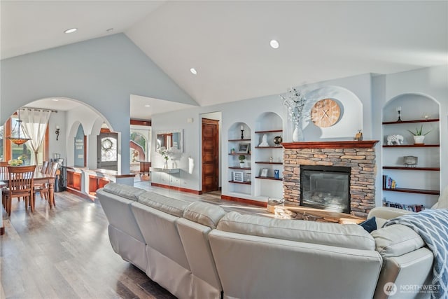 living room featuring high vaulted ceiling, a fireplace, built in features, and wood finished floors