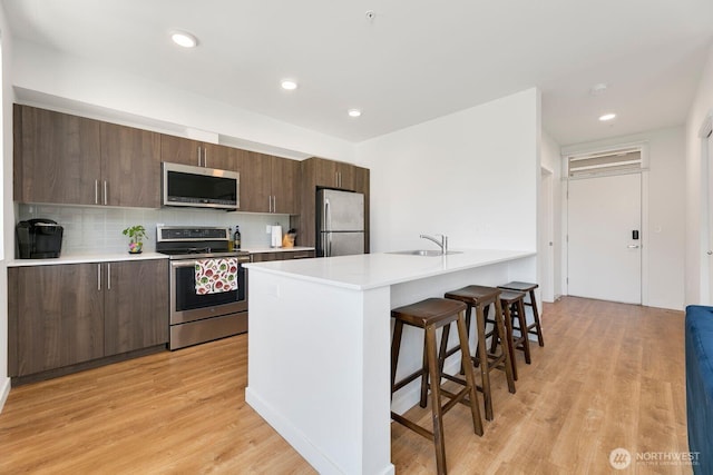 kitchen featuring a breakfast bar area, a sink, light countertops, appliances with stainless steel finishes, and light wood-type flooring