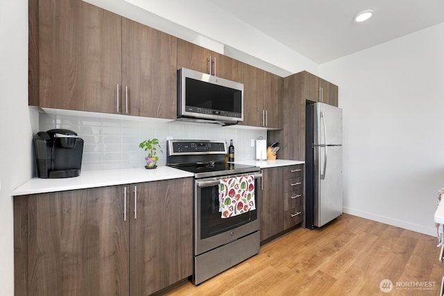 kitchen with baseboards, decorative backsplash, appliances with stainless steel finishes, light countertops, and light wood-type flooring