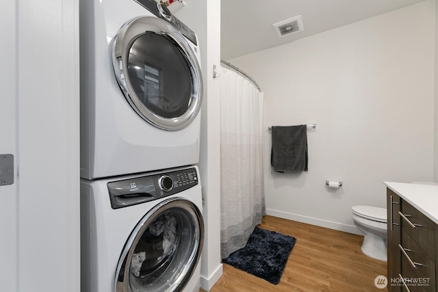 laundry area featuring laundry area, visible vents, baseboards, light wood finished floors, and stacked washer and clothes dryer