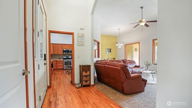 living room featuring ceiling fan with notable chandelier, a high ceiling, arched walkways, and light wood finished floors