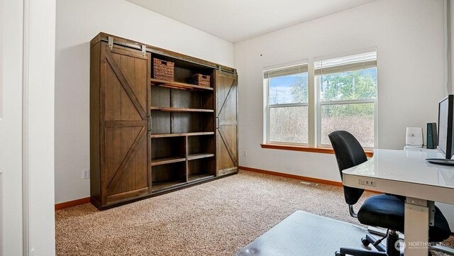 office with a barn door, baseboards, and light carpet